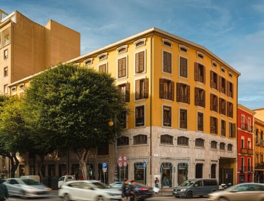 Edificio giallo a Cagliari, Sardegna, con auto in movimento. Architettura urbana tipica della città, ideale per viaggi e scoperta della cultura locale. Servizi e marketplace per motociclisti a Urban Karalis.
