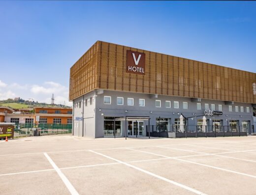 Vista esterna del V Hotel con ampio parcheggio, design moderno e insegna ben visibile, ideale per motociclisti in viaggio.