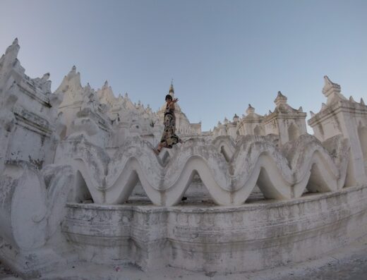 Donna in abito floreale che cammina sull'architettura bianca ondulata di Hsinbyume Pagoda, Mingun, Myanmar, con il cielo azzurro sullo sfondo.