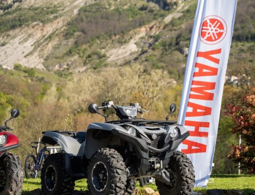 ATV Yamaha grigio in primo piano con bandiera Yamaha e montagna sullo sfondo, ideale per off-road Val di Lima