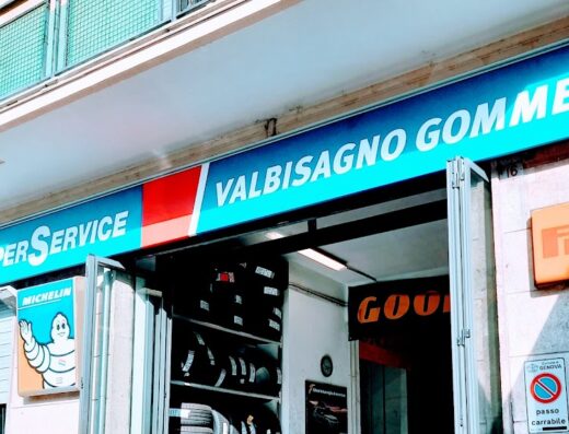 La facciata di Valbisagno Gomme Srl, un centro SuperService gommista a Genova, con insegne di Michelin, Pirelli e GoodYear, e scaffali di pneumatici visibili.