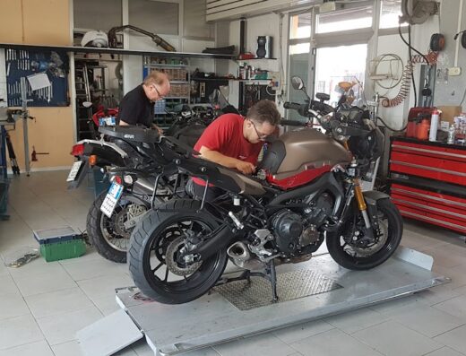 Interno dell'officina Valerio Moto sas, con due meccanici al lavoro su diverse motociclette su un ponte sollevatore. Riparazione e manutenzione moto.