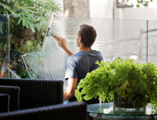 Un uomo pulisce una vetrata con un tergivetro, servizio di pulizia e sanificazione ambientale a Brindisi offerto da Vapor Wash.