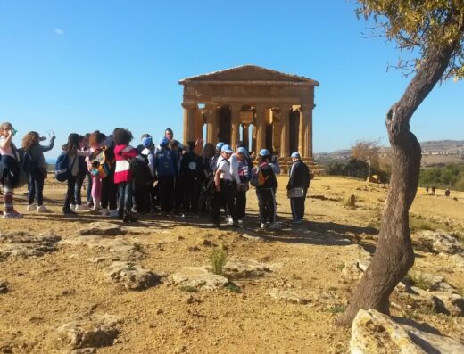 Gruppo di persone in visita al Tempio di Concordia nella Valle dei Templi in Sicilia, con cielo azzurro e un albero in primo piano. Viaggi di Nicle.