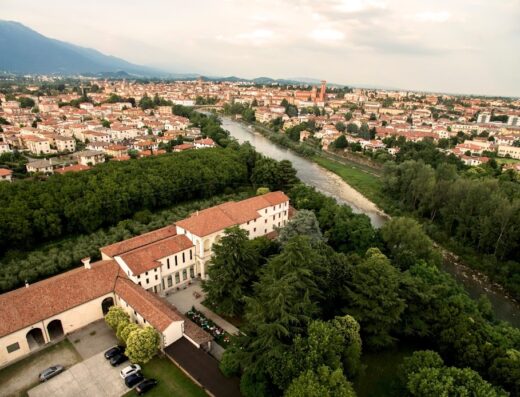 Vista aerea di Villa Angaran San Giuseppe, con il fiume Brenta, il paesaggio urbano di Bassano del Grappa e le montagne sullo sfondo.