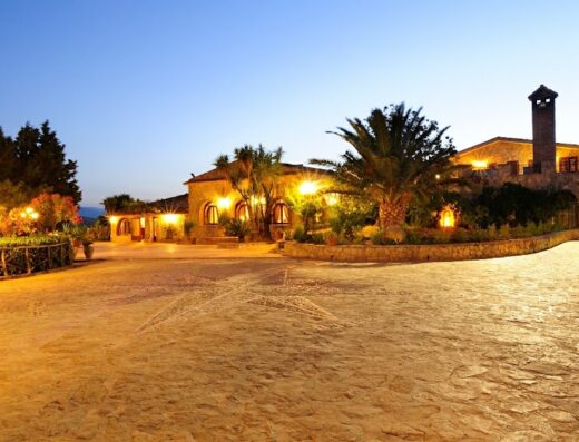 Villa Dafne di sera, elegante struttura ricettiva con giardino illuminato, palme e architettura in pietra, atmosfera accogliente per vacanze e relax.