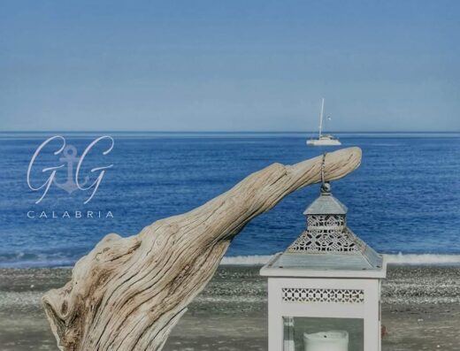Decorazione marittima a VILLA G&G CALABRIA con legno, lanterna bianca e barca a vela sullo sfondo. Un'atmosfera di relax e bellezza.