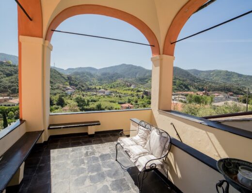 Terrazza panoramica di Villa L'Amandola con vista sulle colline liguri. Archi, panche e cuscini per un relax esclusivo in Liguria.
