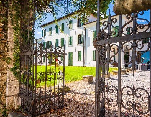 Villa Policreti: cancello in ferro battuto aperto sul giardino con prato verde e facciata bianca della villa con persiane verdi.