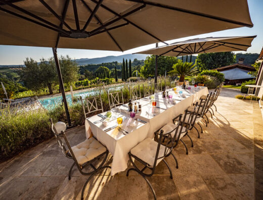 Tavolo imbandito per pranzo all'aperto a Villa Rey Countryhouse, con vista panoramica sulla campagna toscana e piscina.