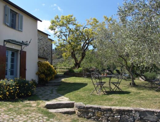 Tranquillo giardino italiano a Villanova con prato verde, tavolo in ferro battuto, ulivi e una casa di campagna in pietra.