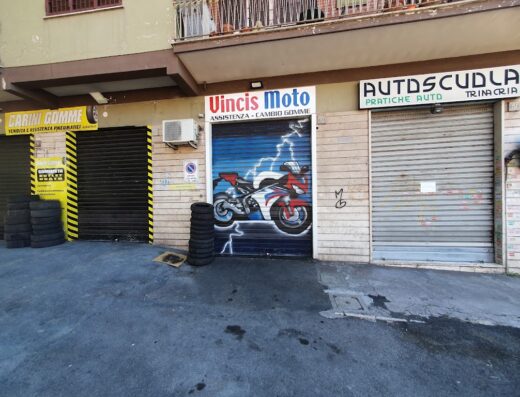 Vincismoto, negozio di assistenza e cambio gomme per moto con saracinesca decorata con un'illustrazione di una moto sportiva rossa e bianca.