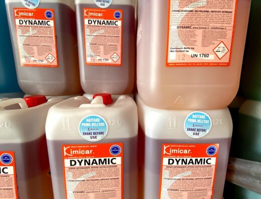 Scaffale con taniche di detergente autolucidante Kimicar Dynamic da 12 litri, prodotto per la cura e pulizia di moto e veicoli, disponibile da Vittorio Di Maria Srl