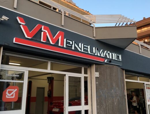 Facciata di VM Pneumatici, negozio specializzato in pneumatici per moto e servizi di manutenzione, con insegna ben visibile e auto all'interno.