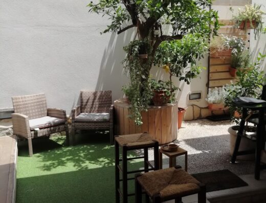 Patio esterno di V&V Suite & Breakfast con sedie in vimini, sgabelli in legno e albero di limone in vaso, ideale per rilassarsi all'aperto.