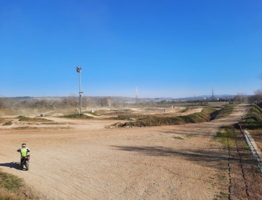 Vista del Wafna MotoPark con un motociclista che guida una moto da cross su un percorso sterrato sotto un cielo azzurro. Servizi e accessori per motociclisti disponibili.