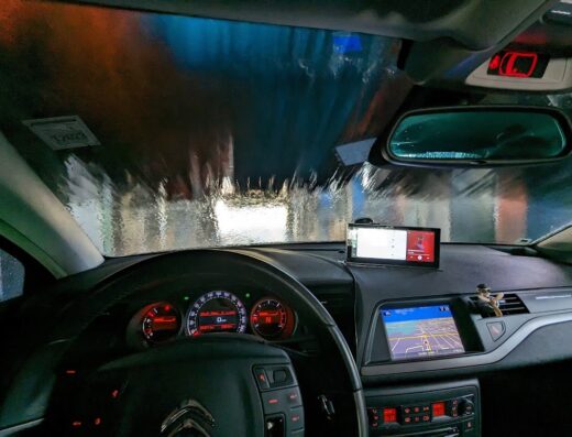 Interno di un'auto durante il lavaggio presso Wash Is Now S.r.l., con vista sul cruscotto, il navigatore GPS e le spazzole del lavaggio auto.