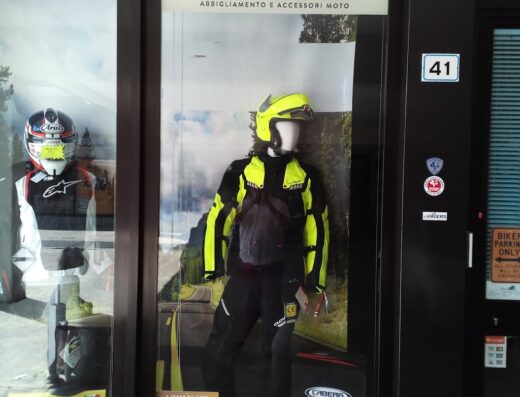 Vetrina del negozio We Riders a Siena, con abbigliamento e accessori moto esposti, inclusi caschi Arai e Caberg, giacche e pantaloni tecnici.