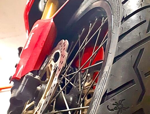 Primo piano di una moto rossa di WESPART 59 SNC MOTORIPARAZIONI che mostra il pneumatico anteriore, il disco freno e parte della carrozzeria.