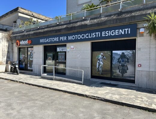 Wheelup megastore per motociclisti esigenti, negozio di accessori moto e abbigliamento tecnico. Moto parcheggiata di fronte all'ingresso.