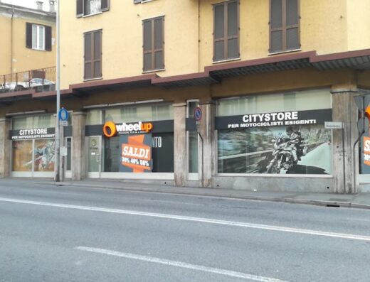 Foto della vetrina del negozio Wheelup, rivenditore di accessori e abbigliamento per motociclisti, con insegne "CITYSTORE" e promozioni di sconti