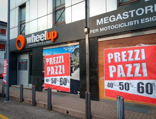 Foto del negozio Wheelup, megastore per motociclisti, con insegna luminosa e promozioni 'Prezzi Pazzi' del 40% al 60%.