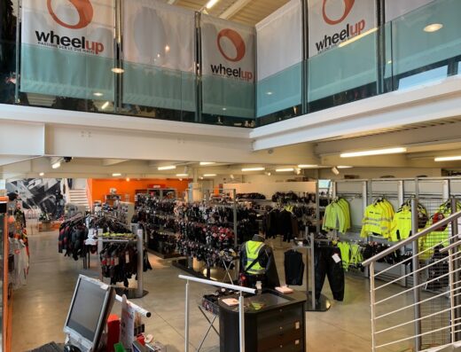 Interno del negozio Wheelup, con espositori di abbigliamento e accessori moto, caschi, giacche ad alta visibilità e il logo del negozio.