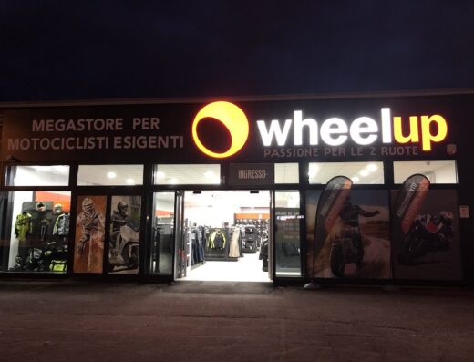 Wheelup, megastore per motociclisti esigenti: negozio di accessori e abbigliamento moto. Vetrina con caschi, tute, giacche e banner promozionali.