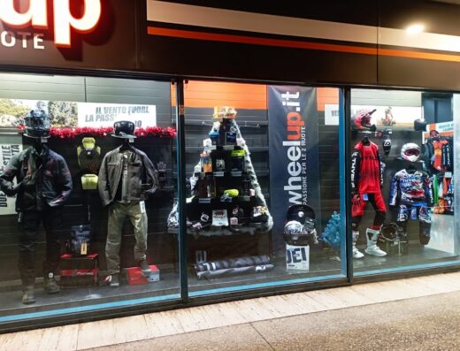 Vetrina del negozio Wheelup con esposizione di abbigliamento e accessori moto, caschi, giacche, protezioni e completi da cross, con decorazioni natalizie.