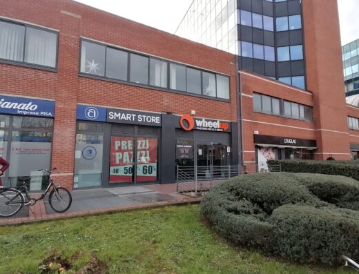 Foto del negozio Wheelup, marketplace per motociclisti, situato in un edificio di mattoni accanto a un Smart Store e Douglas. Wheelup offre accessori e servizi per moto e viaggi in moto.