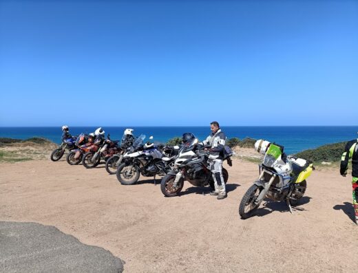Gruppo di motociclisti con moto da turismo adventure in sosta con vista mare in Sardegna durante un tour esperienziale.
