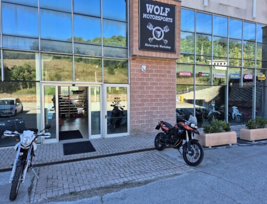 Ingresso di Wolf Motorsports, officina specializzata in moto e accessori. In primo piano, moto adventure e da enduro parcheggiate. Vetrine con marchi come Motul, Akrapovic, Brembo e Givi.