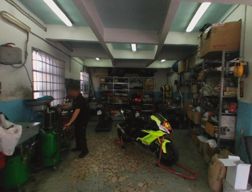 Interno dell'officina Xcar di Barbieri Roberto e Mazzoli Flavio a Bologna, con moto sportiva gialla su cavalletto, meccanico al lavoro e scaffali pieni di accessori e ricambi moto.