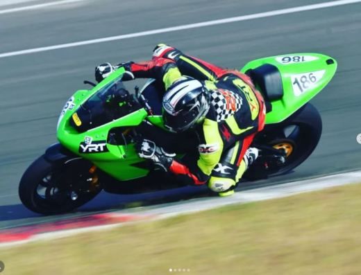 YURIMOTO Di Belotti Yuri A.: Immagine di un motociclista in sella a una moto verde da corsa, numero 186, su un circuito. Abbigliamento tecnico da gara.