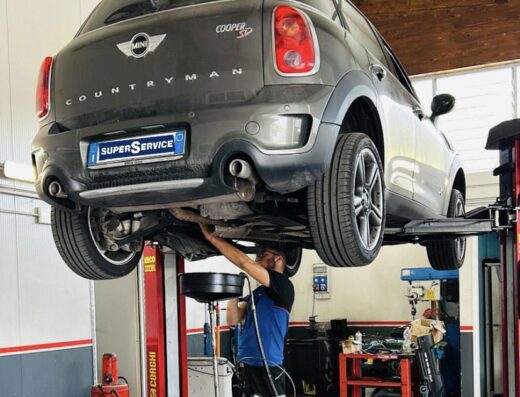 Auto Mini Countryman grigia sollevata su un ponte in officina meccanica durante un intervento di manutenzione da parte di un meccanico.