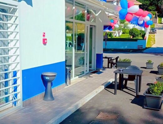 Esterno del bar Emma, con decorazioni di palloncini rossi, bianchi e blu, tavolini all'aperto e insegna ben visibile. Luogo accogliente per una pausa durante un viaggio in moto.